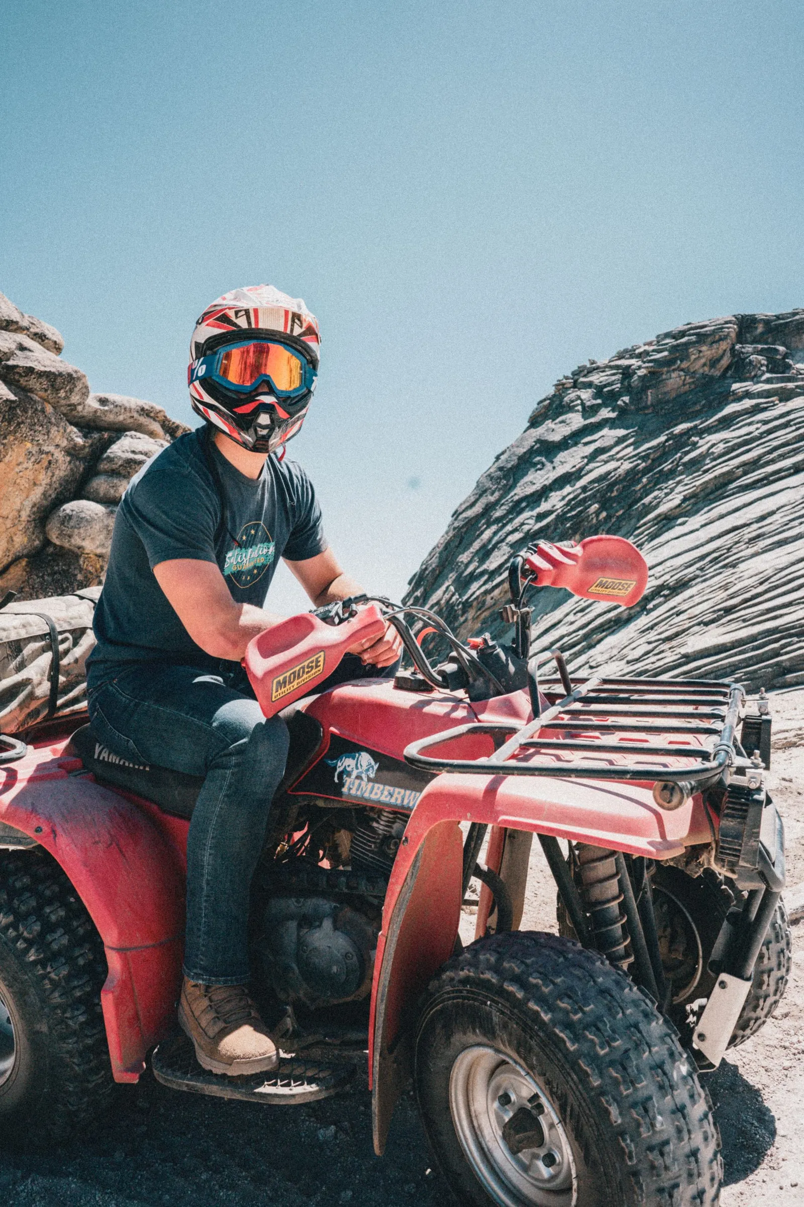 Helmeted rider on a red quad on rocky ground at Bass Lake, California